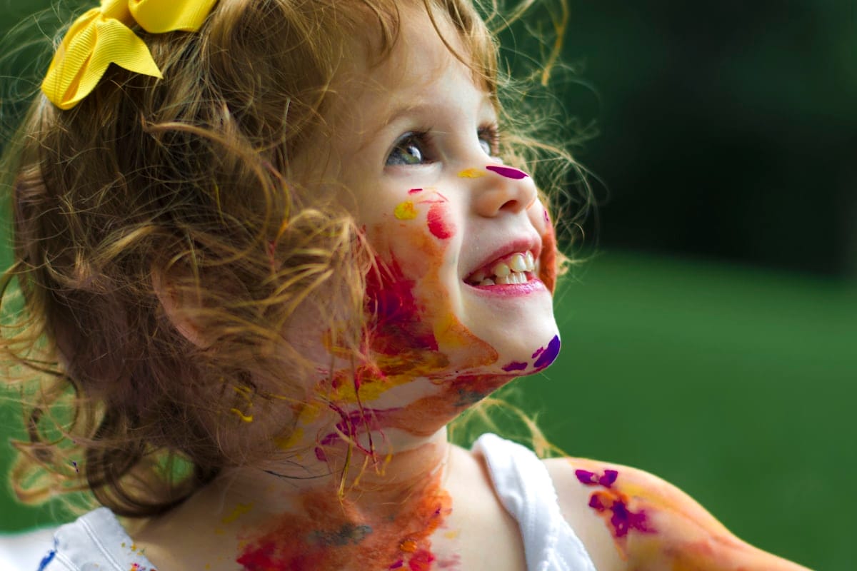Petite fille souriante le visage couvert de peinture colorée